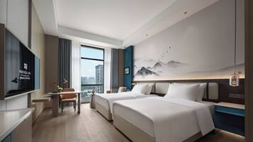 Habitación de hotel con cama, escritorio, silla, televisión y ventana grande.
