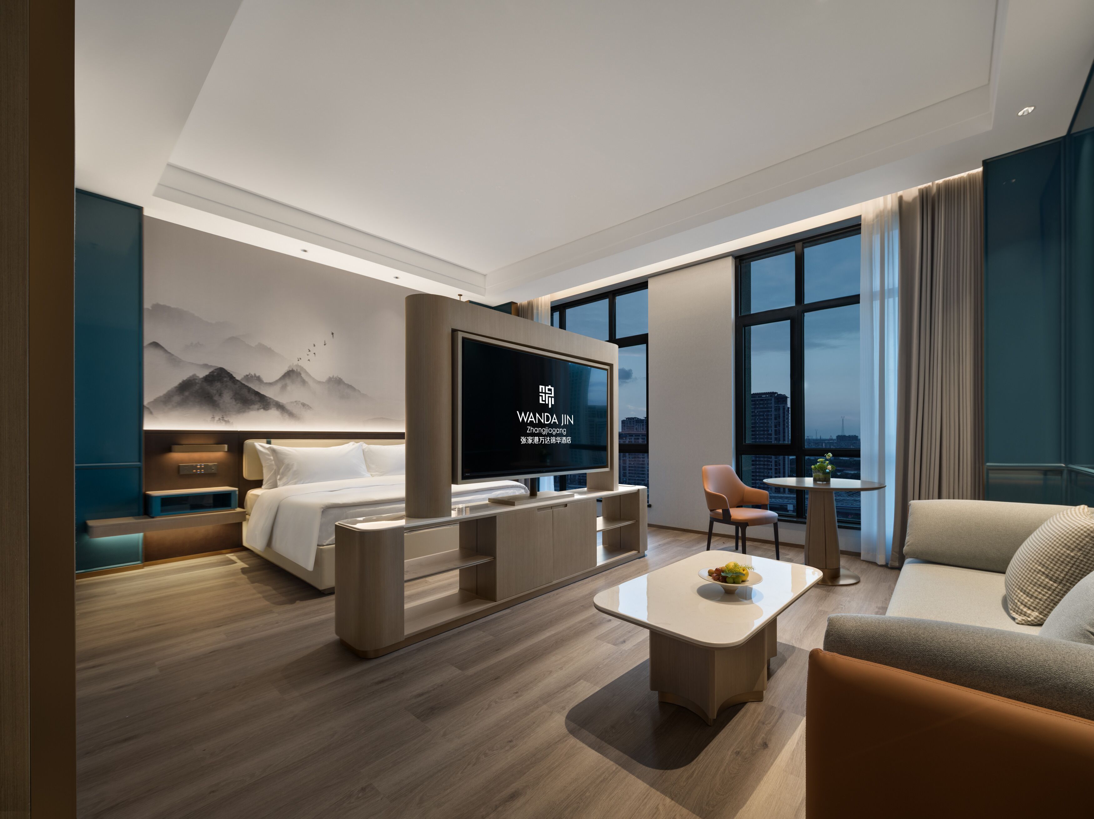 Quarto de hotel moderno com cama, televisão, sofá, mesa de centro e vista para a cidade.