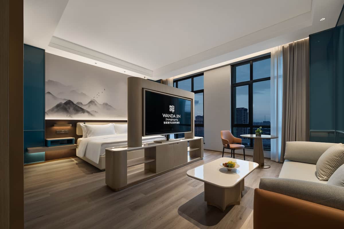 Una habitación de hotel moderna con cama, televisor, sofá, mesa de centro y vista a la ciudad.