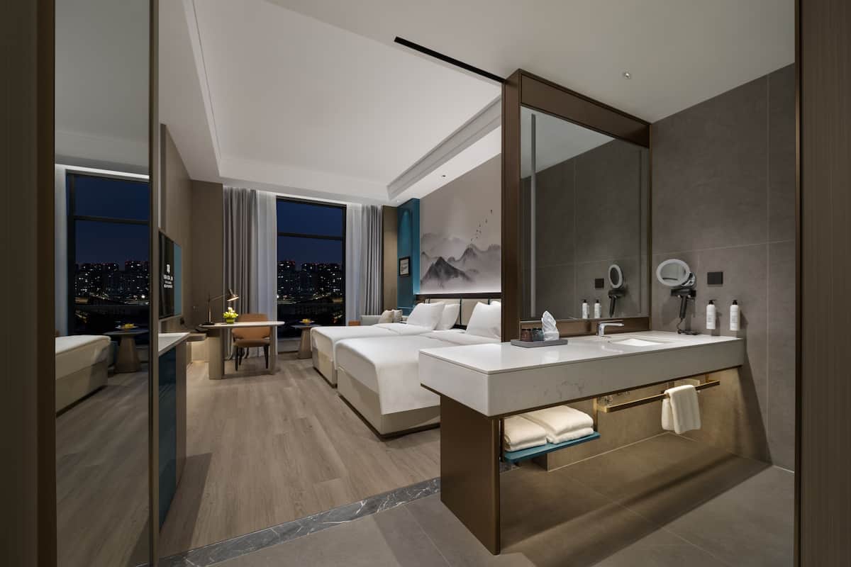 Una habitación de hotel moderna con una cama grande, un escritorio, un baño con tocador y vistas a la ciudad.