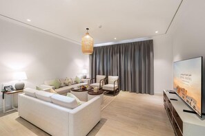 A modern living room with a sofa, chairs, a coffee table, a TV, and a large window with curtains. - Mina Hotel And Residences (Doha)
