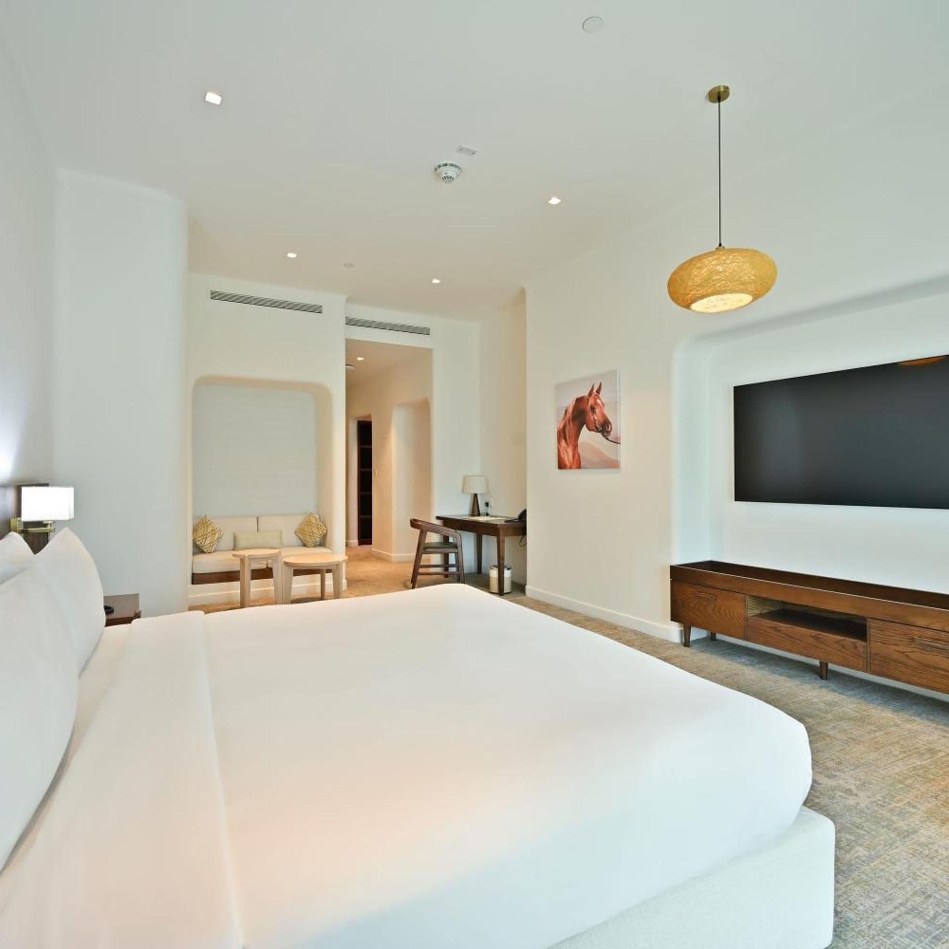 Una habitación de hotel moderna con una cama grande, un escritorio, una silla, un televisor y una lámpara colgante.