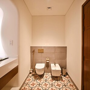 A bathroom with two toilets, a shower, and a sink. - Mina Hotel And Residences (Doha)