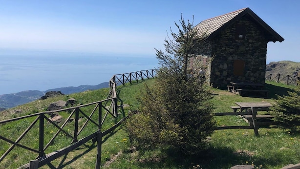 En stenhytte med et picnicbord og et træhegn, med udsigt over et bjergrigt landskab.