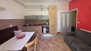 En kompakt opholdsstue med tekøkken, spiseplads med bord og stole, samt en sofa.