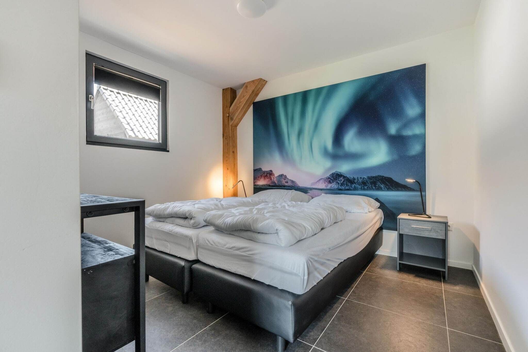 Un dormitorio moderno con cama, una mesita de noche pequeña, un buró, una ventana con vistas y un mural grande en la pared.