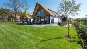 Une maison moderne avec une grande façade vitrée, un toit en pente et une pelouse bien entretenue.