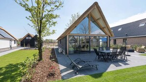 Une maison moderne dotée d’une grande extension en verre, d’un patio avec mobilier d’extérieur et d’une pelouse bien entretenue.