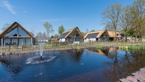 Une rangée de maisons modernes avec des toits inclinés et de grandes fenêtres, un petit étang avec une fontaine et un ciel bleu clair.