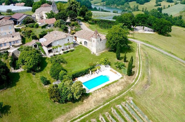 An aerial view of a property with a swimming pool, a church, and surrounding fields.