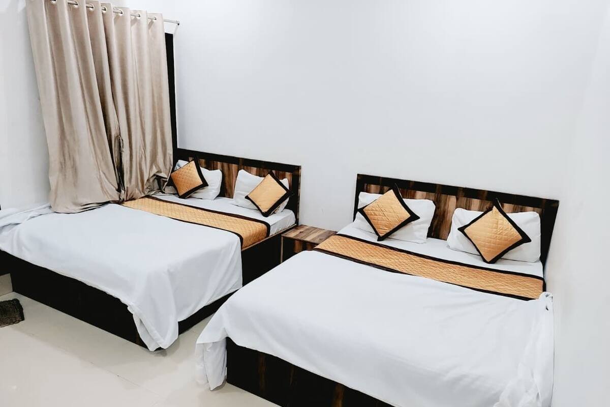 Deux lits simples avec des têtes de lit en bois, du linge de lit blanc et des coussins décoratifs.