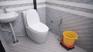 Ein Badezimmer mit Toilette, Waschbecken und einem gelben Eimer auf einem roten Gestell.