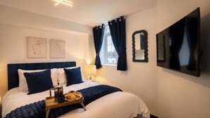 Habitación de hotel con cama, mesita de noche con cafetera, bandeja de desayuno y una obra de arte en la pared.