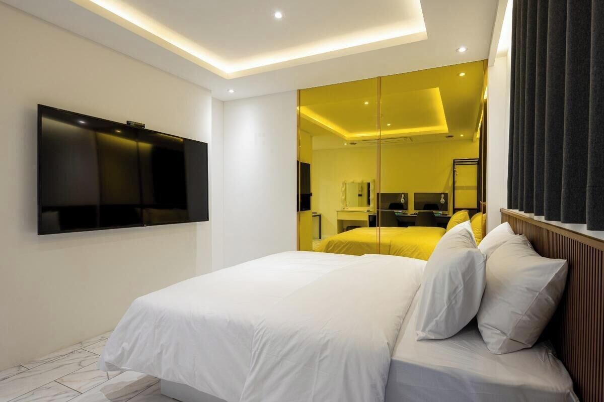 A modern hotel room with a large bed, a flat-screen TV mounted on the wall, and a mirror reflecting the room.