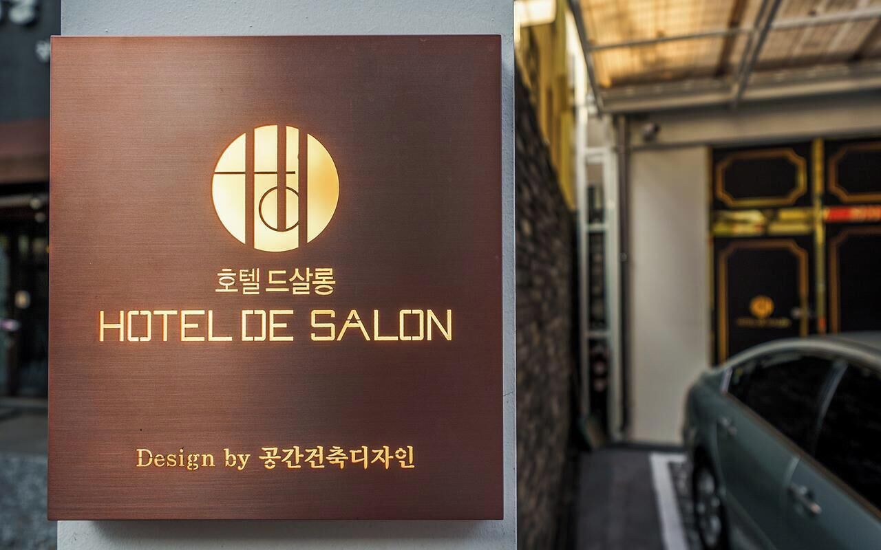 Placa indicando o Hotel De Salon, com design minimalista e um carro estacionado ao fundo.