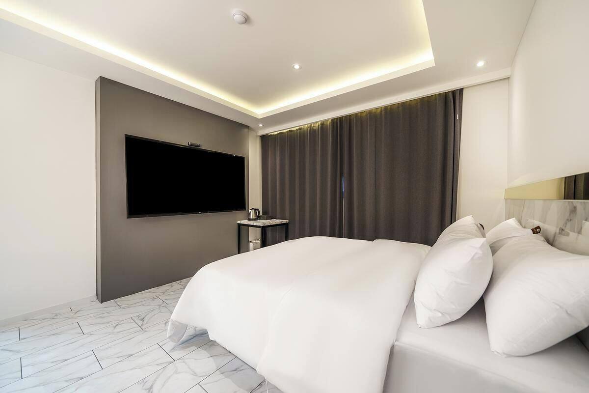 Una camera d'albergo moderna con un letto grande, una TV a schermo piatto, un comodino e un'ampia finestra con tende.