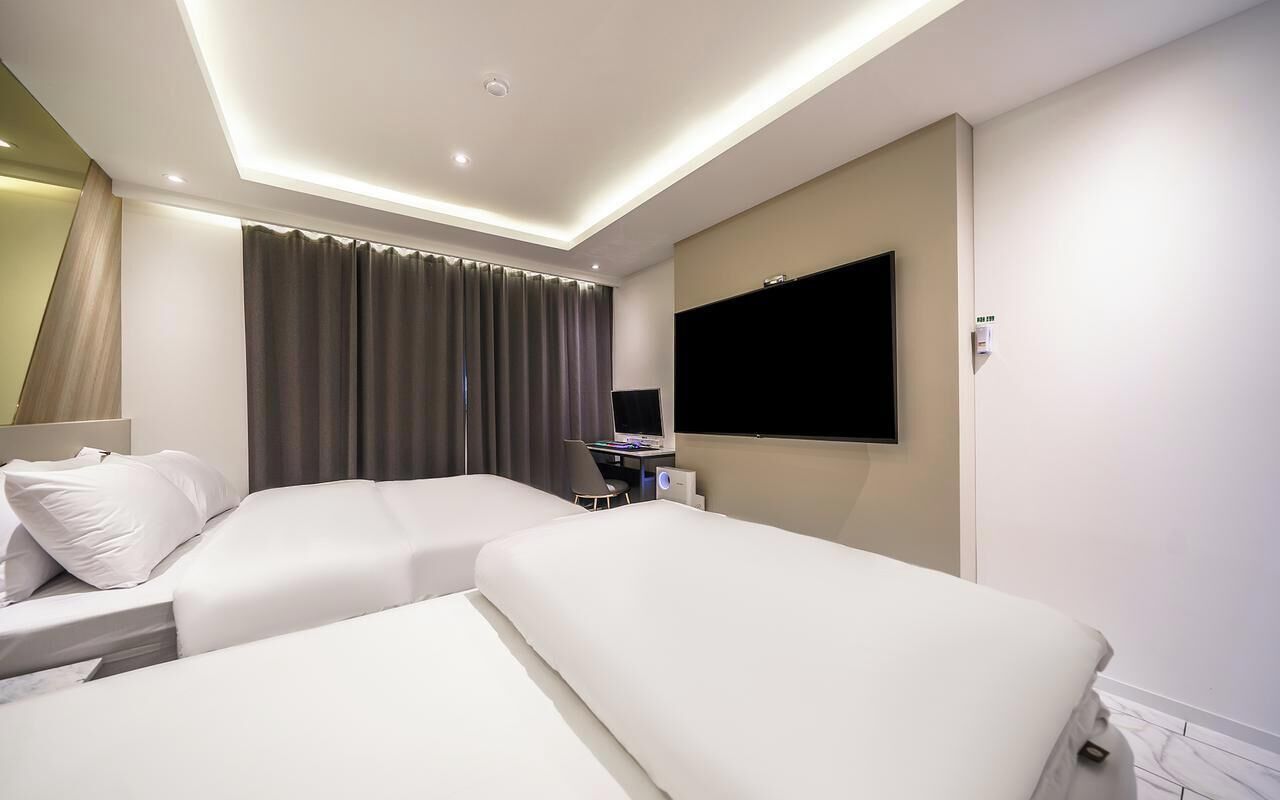 Habitación de hotel con dos camas, un escritorio, un televisor de pantalla plana y un ventanal con cortinas.