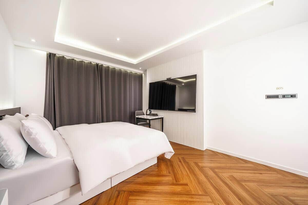 Una camera d'albergo moderna con un letto grande, una scrivania, una sedia, una TV e un pannello di controllo.