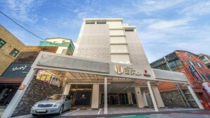 Un hotel con fachada moderna, acceso cubierto y estacionamiento visible.