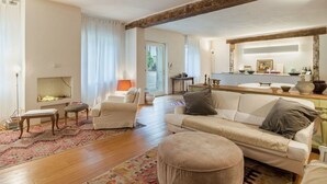 A spacious living room with a large sofa, a coffee table, and a patterned rug. There is a wooden beam on the ceiling, a fireplace, and a dining area visible through an open door. - Apartment in Camaiore with 2 bedrooms sleeps 4 (Camaiore)