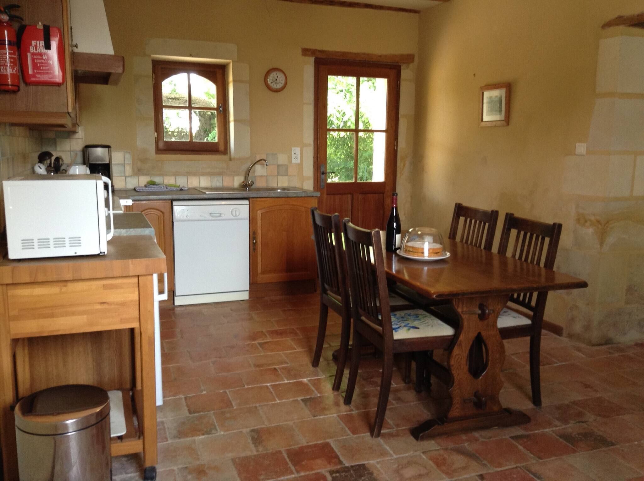 Una cucina con un forno a microonde bianco, una lavastoviglie, un lavello e sedie di legno attorno a un tavolo.