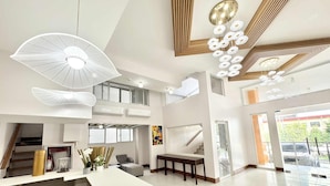 A spacious living area with a long white table, a gray sofa, and a wooden bench. There are multiple air conditioning units on the ceiling, and a large window provides natural light. - Palette Cebu The Almonds Boutique Aparthotel Near University of Cebu (Cebu City)