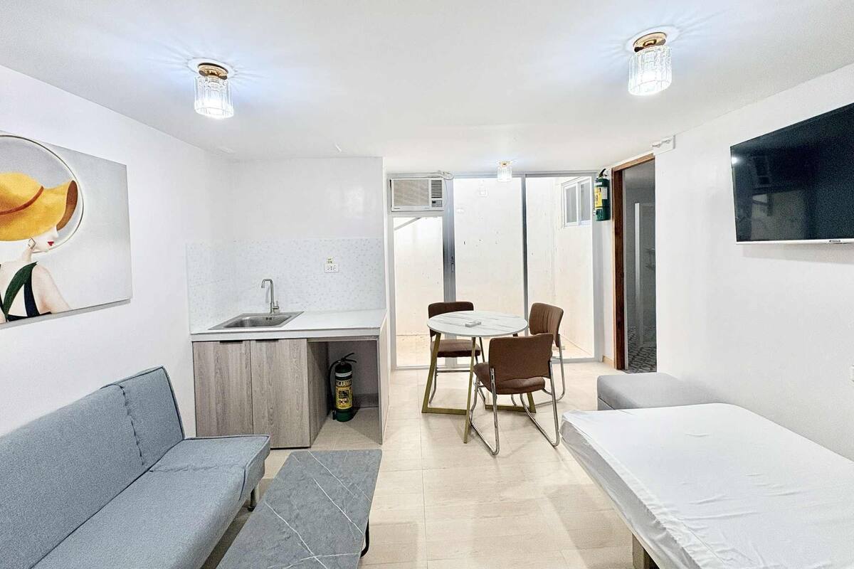 A compact room with a kitchenette, a dining table with chairs, a sofa, and a bed.