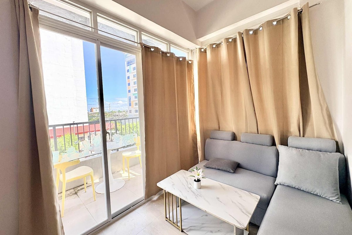 A modern living room with a sofa, a small table, and a view of a balcony with yellow chairs.