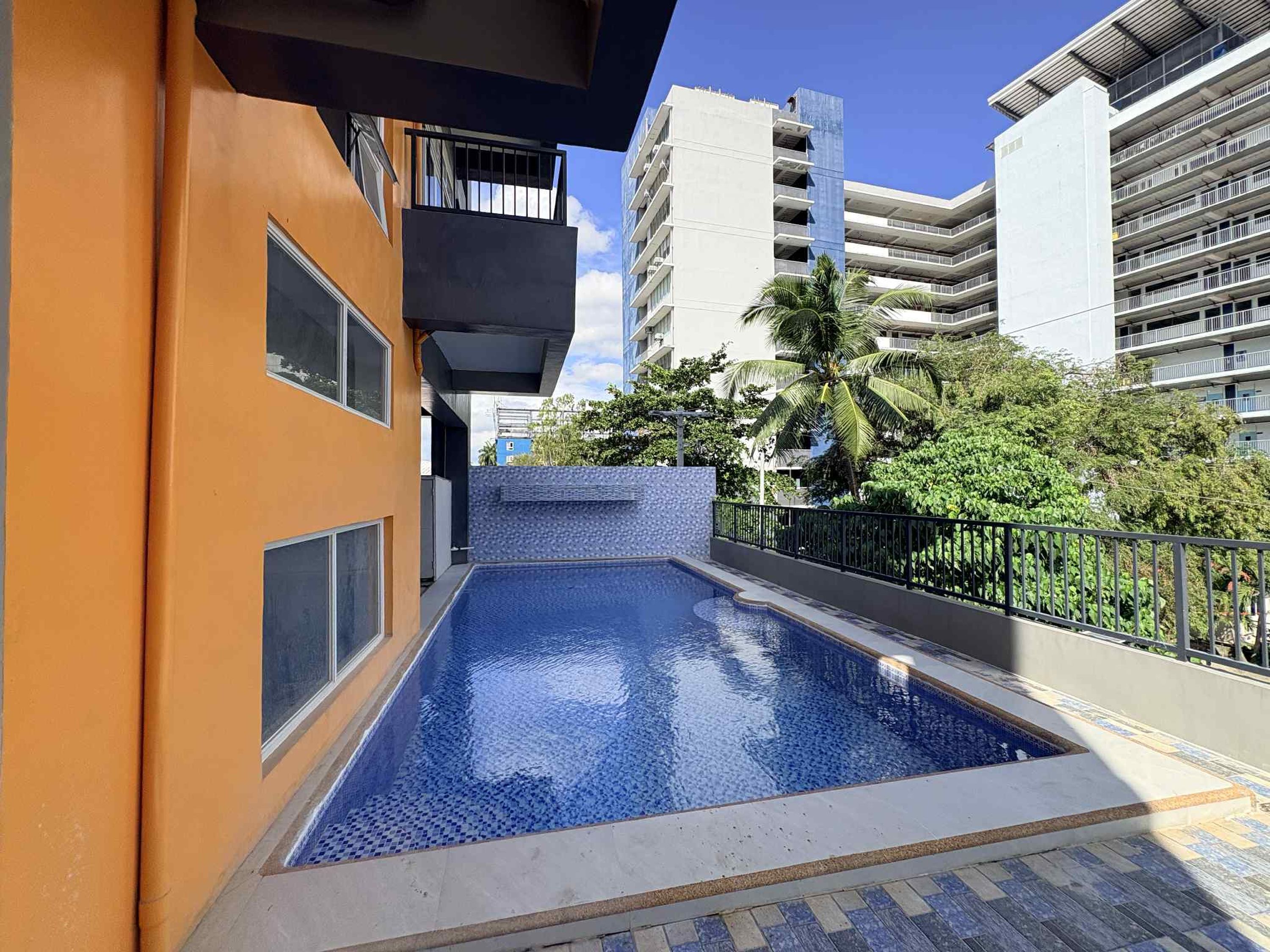 A residential building with a swimming pool, balconies, and a view of surrounding high-rise buildings.