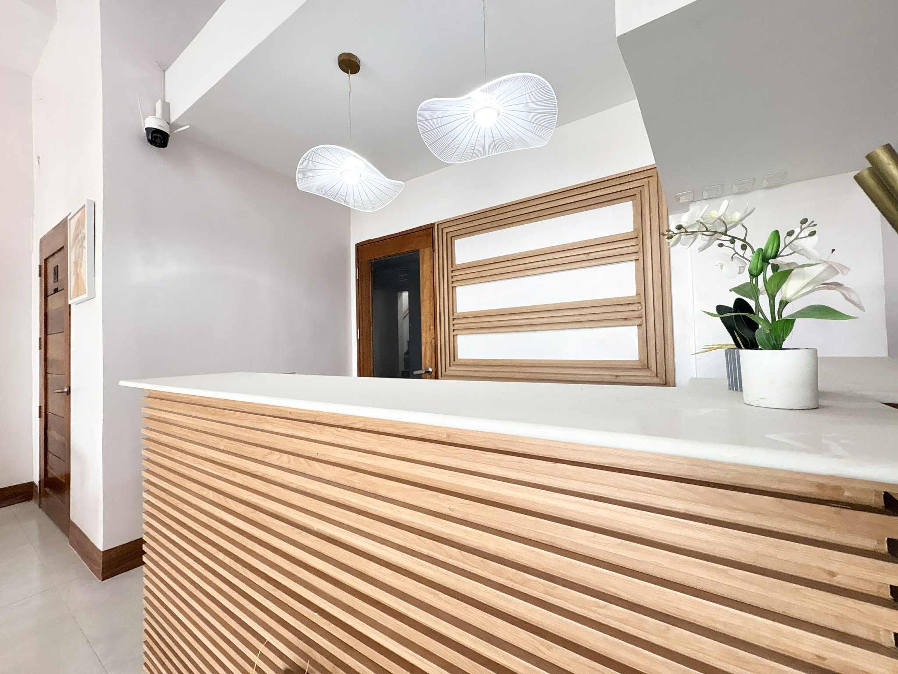 Un comptoir d'accueil avec un design à lattes de bois, un plan de travail blanc, un ventilateur de plafond et une plante en pot.