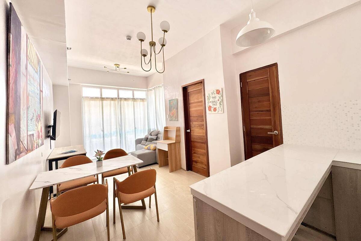 A modern kitchen with a white countertop, wooden cabinets, and a dining area with orange chairs and a table.