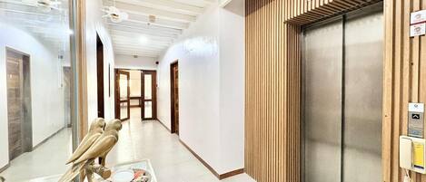 A hallway with a wooden panel wall, an elevator, and a glass door on the left.