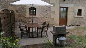 Une terrasse extérieure avec une table ronde et des chaises, un barbecue et une poubelle.