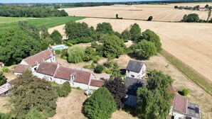 Vue aérienne d’une propriété rurale comprenant plusieurs bâtiments, dont une grande maison avec un toit en tuiles et une construction plus petite équipée d’un panneau solaire.