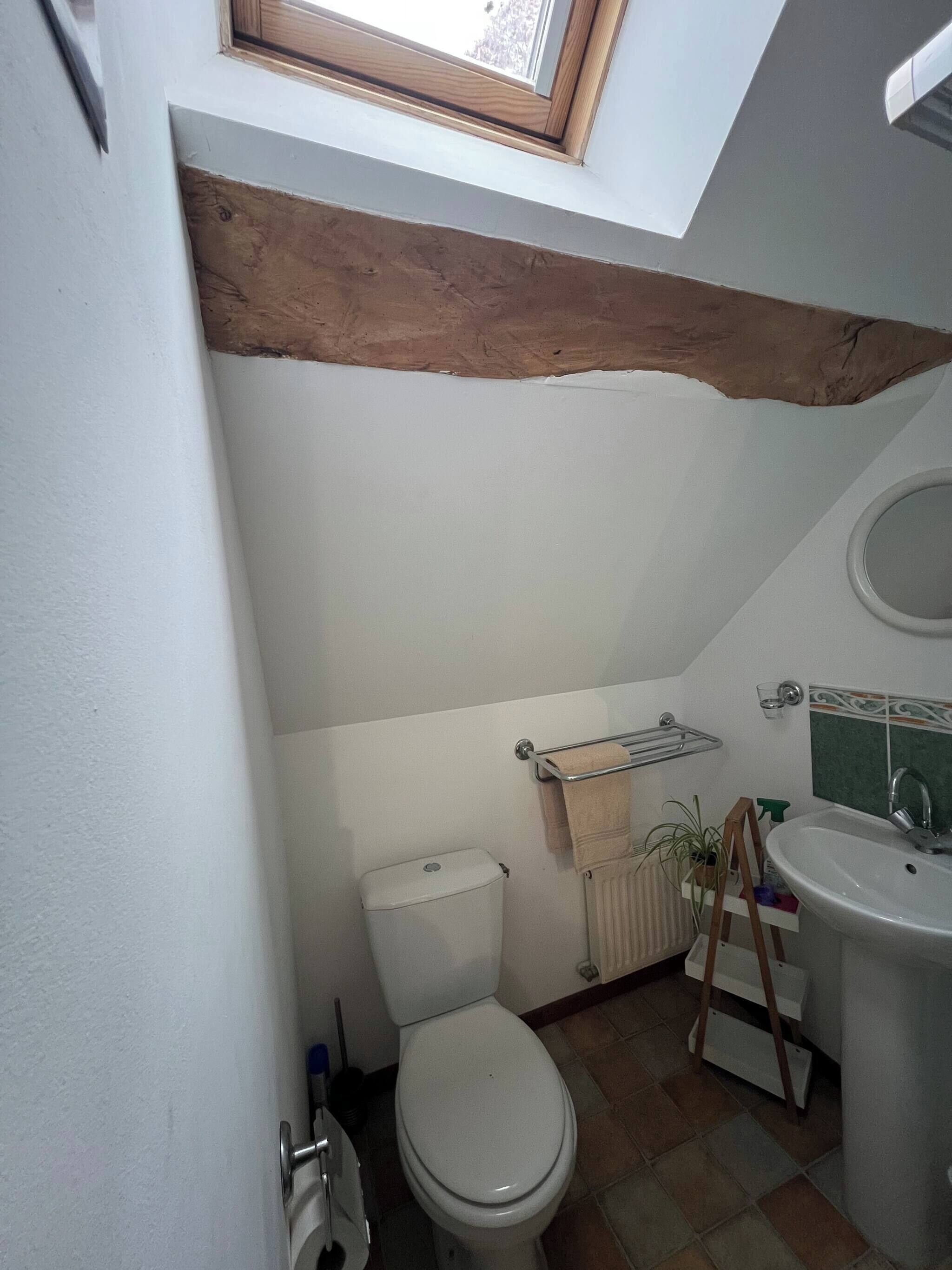 Ein kleines Badezimmer mit Toilette, Waschbecken und Handtuchhalter. Über der Toilette befindet sich ein Oberlicht.