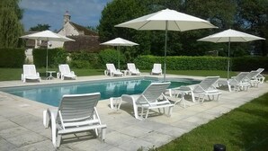 Ein Swimmingpool mit weißen Liegestühlen und Sonnenschirmen, umgeben von Grünflächen und einem Gebäude im Hintergrund.