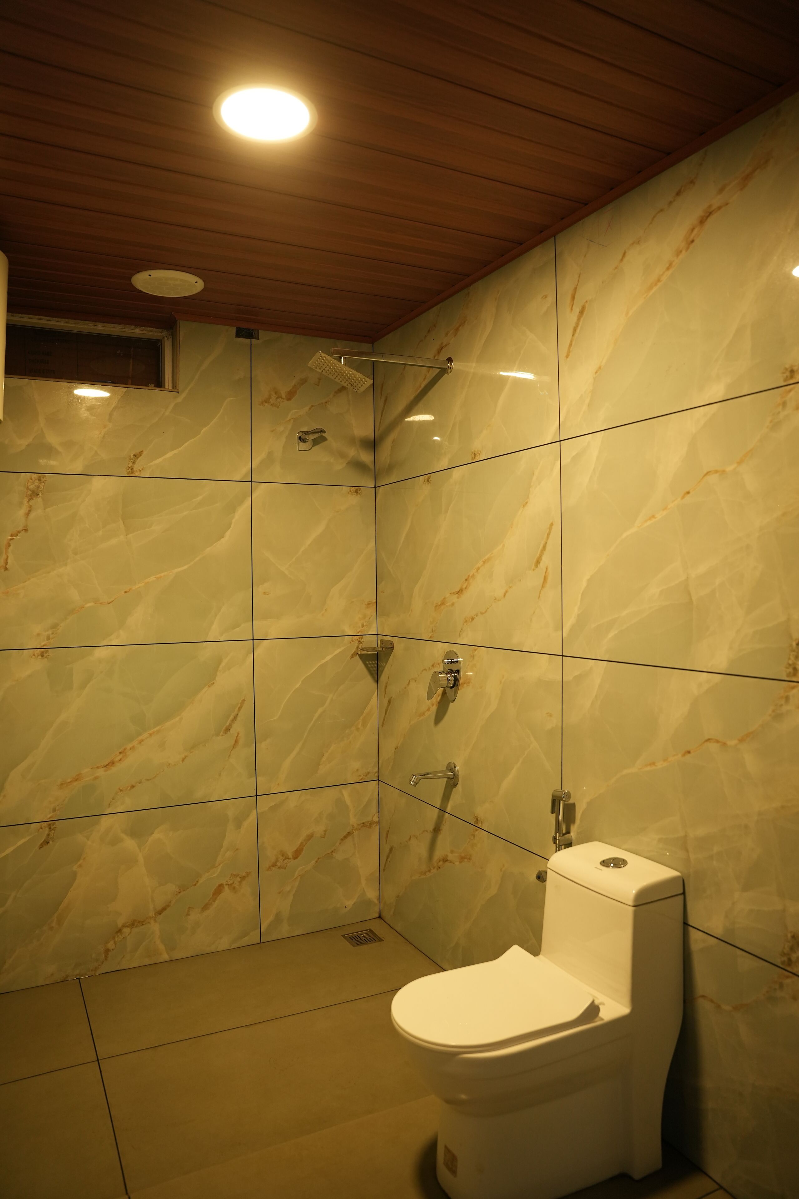 Un baño con pared de mármol, inodoro blanco y ducha.