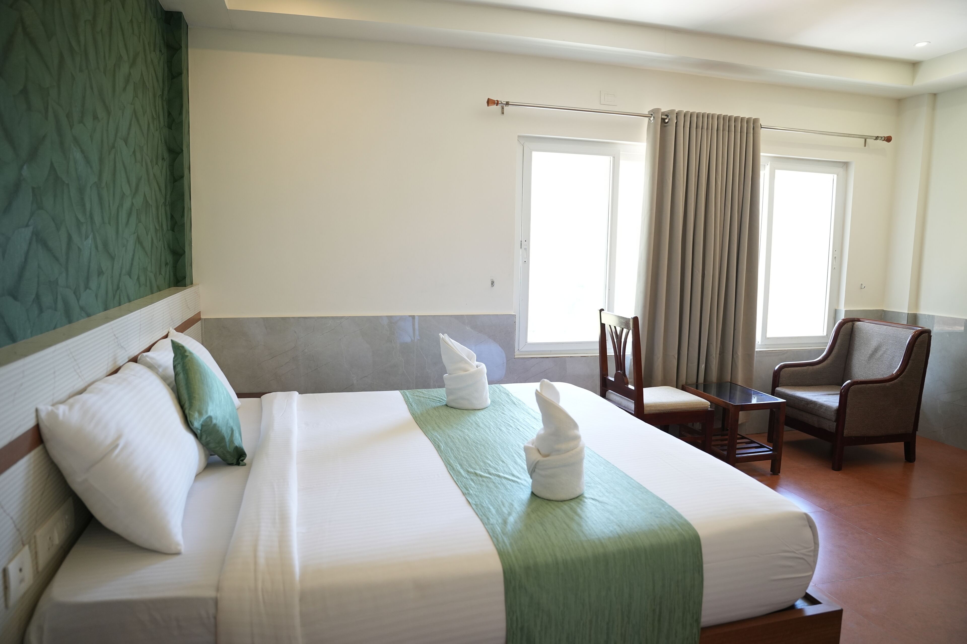 A hotel room with a large bed, a chair, a small table, and a window with curtains.