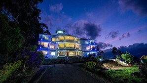 A multi-story building with balconies, surrounded by trees and a well-maintained lawn. - Shola Heaven (Devikolam)