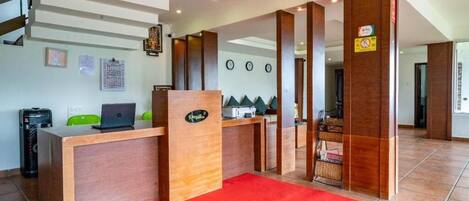 A reception area with a wooden desk, a red carpet, and a staircase in the background.
