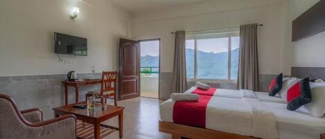 Habitación de hotel con cama, escritorio, silla, televisor y ventana con vista a las montañas.