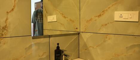 A bathroom with a marble wall, a sink, a mirror, and a trash bin.