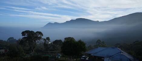 Paisaje rural con una casa, un pequeño jardín y vistas a montañas envueltas en niebla.