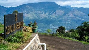 A sign with 'SHOLA HAZAR' written on it, surrounded by greenery and mountains in the background. - Shola Heaven (Devikolam)