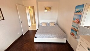 Une chambre à coucher avec un lit, une porte donnant sur une autre pièce et un mur orné d’un tableau encadré.