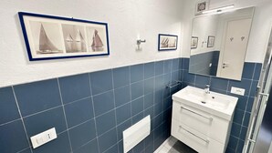 Une salle de bain avec des carreaux bleus, un lavabo blanc, un miroir et des tableaux encadrés accrochés au mur.