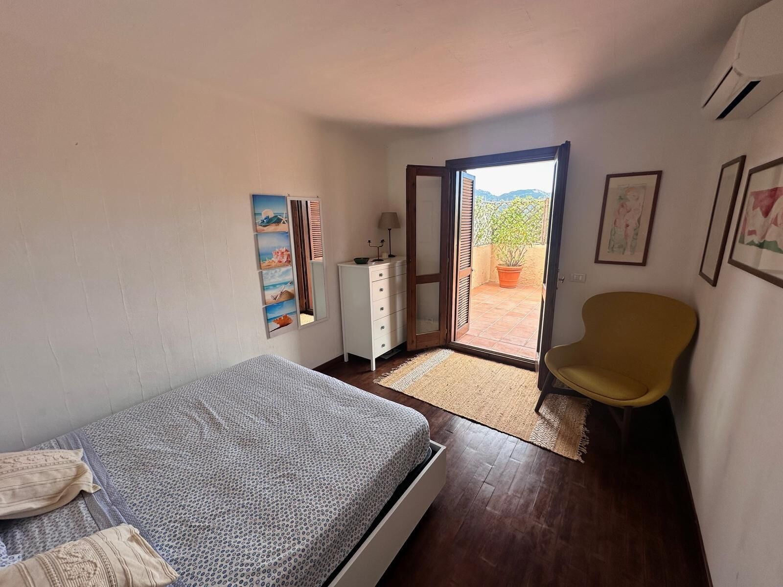 A bedroom with a bed, a dresser, a chair, and a sliding glass door leading to a balcony.