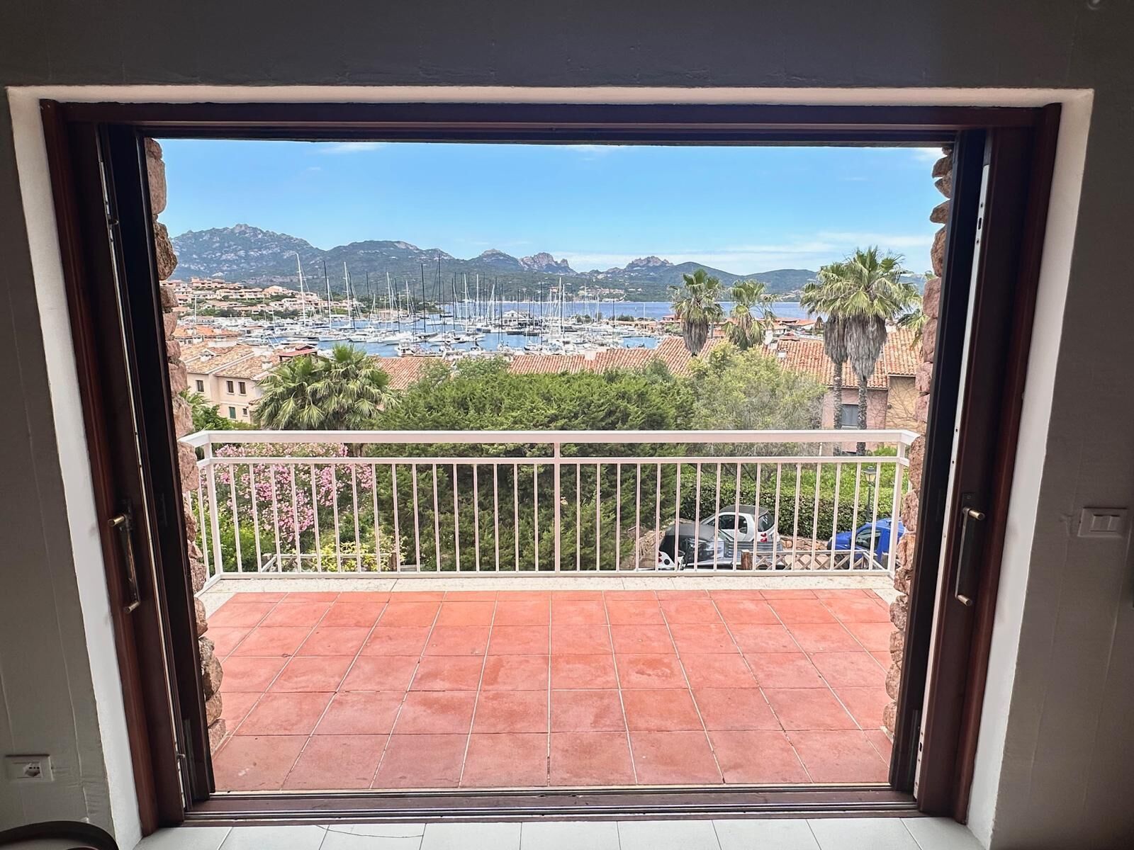 Un balcón con vista a un puerto deportivo, montañas y un pueblo costero.