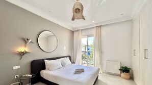 Ein Schlafzimmer mit einem großen Bett, einem runden Spiegel, einem kleinen Tisch und einer Topfpflanze.
