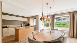 A modern kitchen with a central island, a dining area with a round table, and a view of greenery outside. - Prestigious 5BR Avenue Foch Home - Arc de Triomphe (Paris)